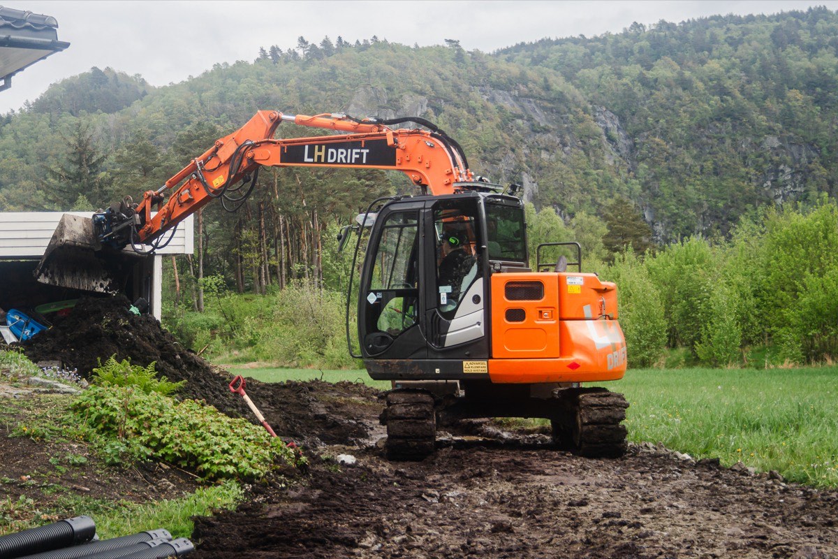 Oransje LH Drift-gravemaskin i arbeid med grunnarbeid på en tomt i Lyngdal.