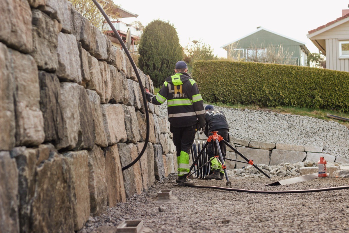To arbeidere fra LH Drift bygger en høy natursteinmur i Lyngdal.